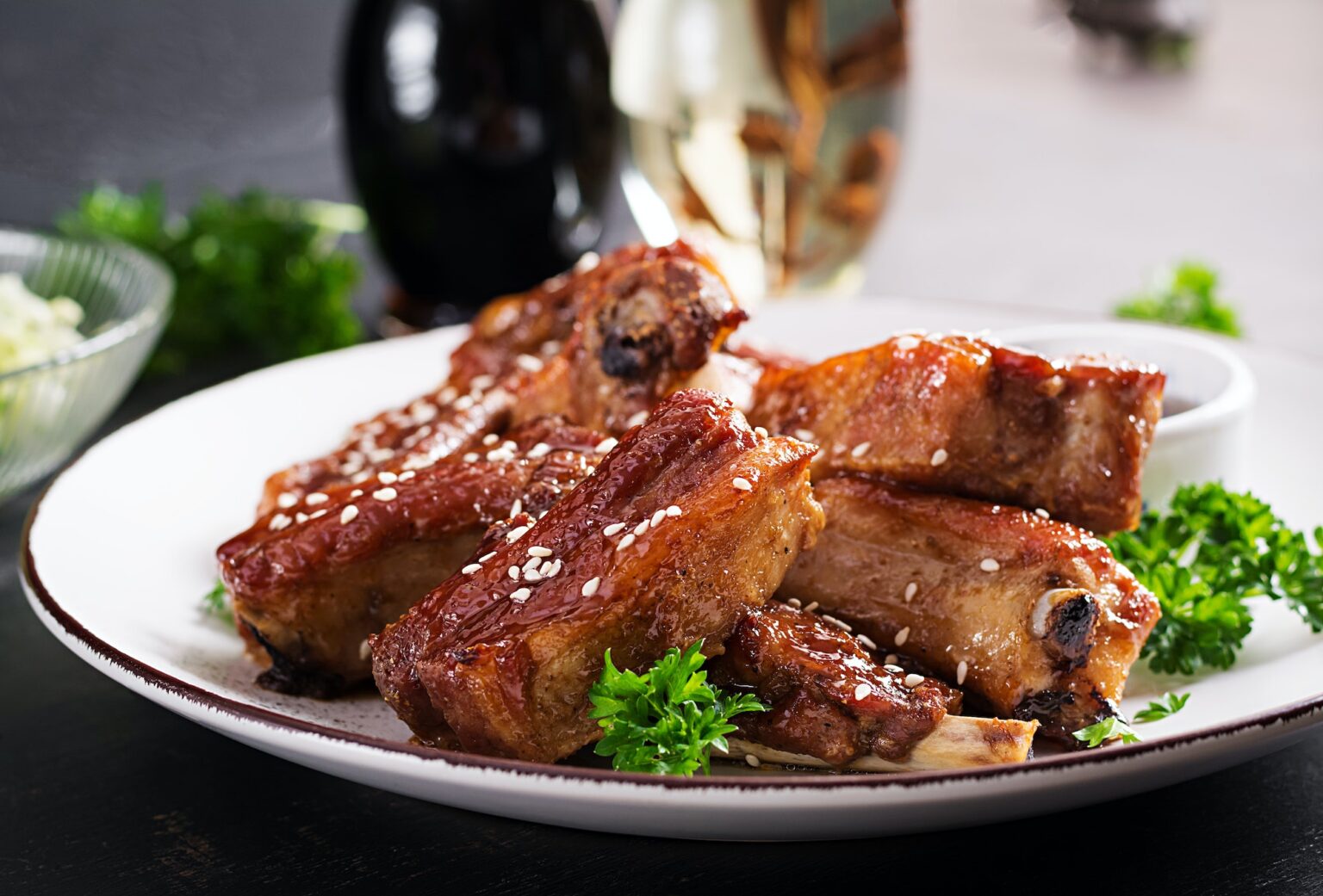 Delicious barbecued spare ribs on plate on dark background. Tasty bbq meat.